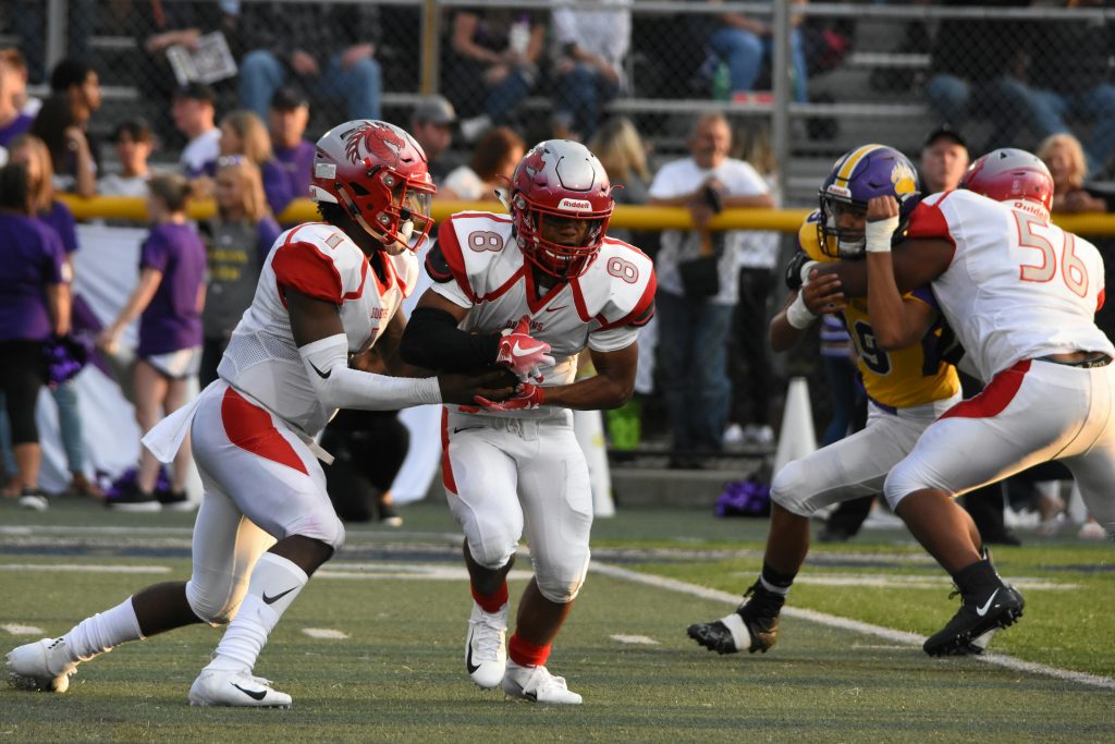 A football player dashes forward, gripping the ball tightly as he races past defenders on the field.