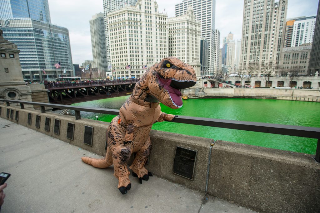 A man wearing a dinosaur outfit stands on a bridge, creating a humorous and imaginative atmosphere.