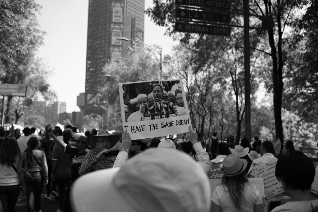 A black and white image depicting a crowd of individuals raising signs, conveying a message of unity and protest.
