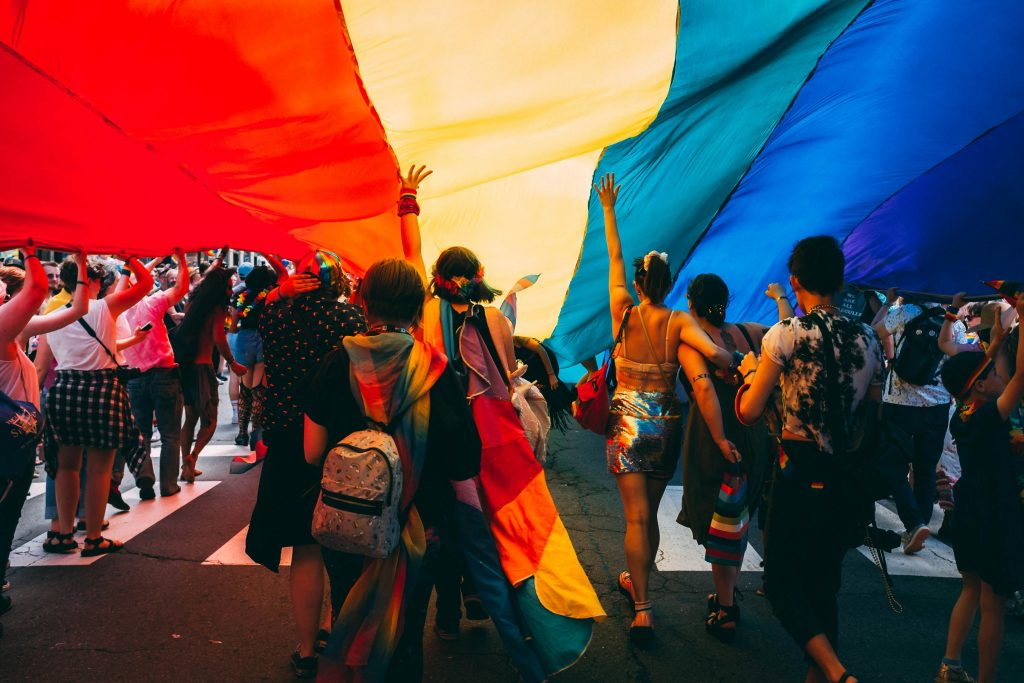 A diverse group of individuals proudly holding rainbow flags while marching together in a vibrant street celebration.