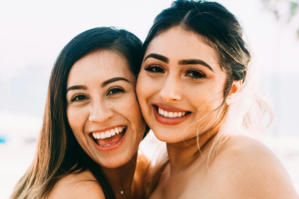Two women with cheerful smiles, posing for the camera, capturing a delightful moment of connection and happiness.