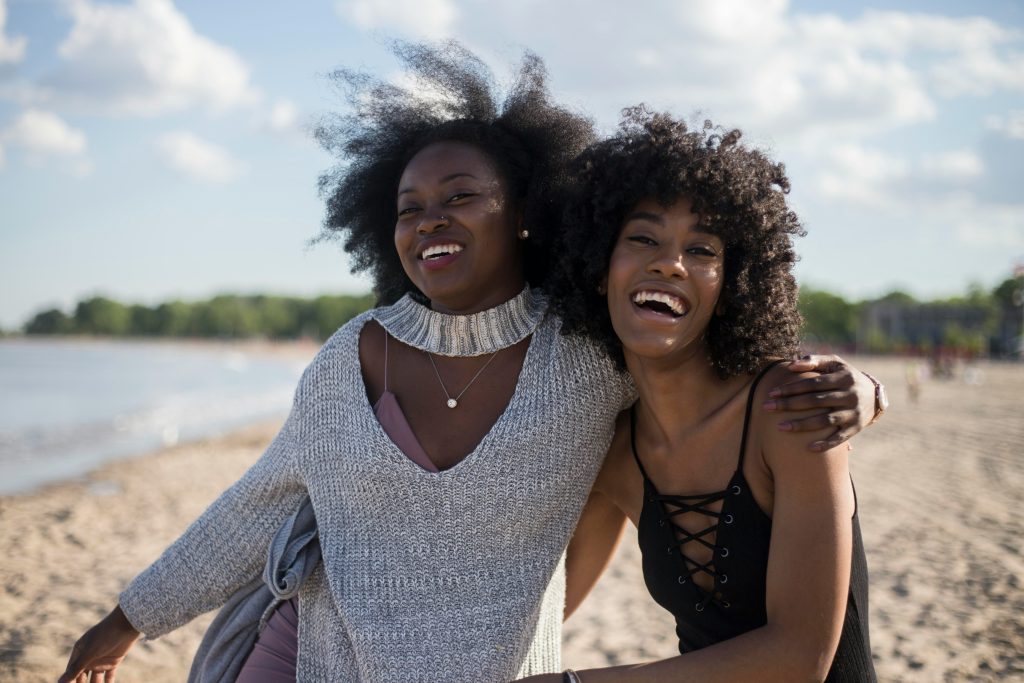 Two women of colour share a moment of laughter and smiles on the beach.