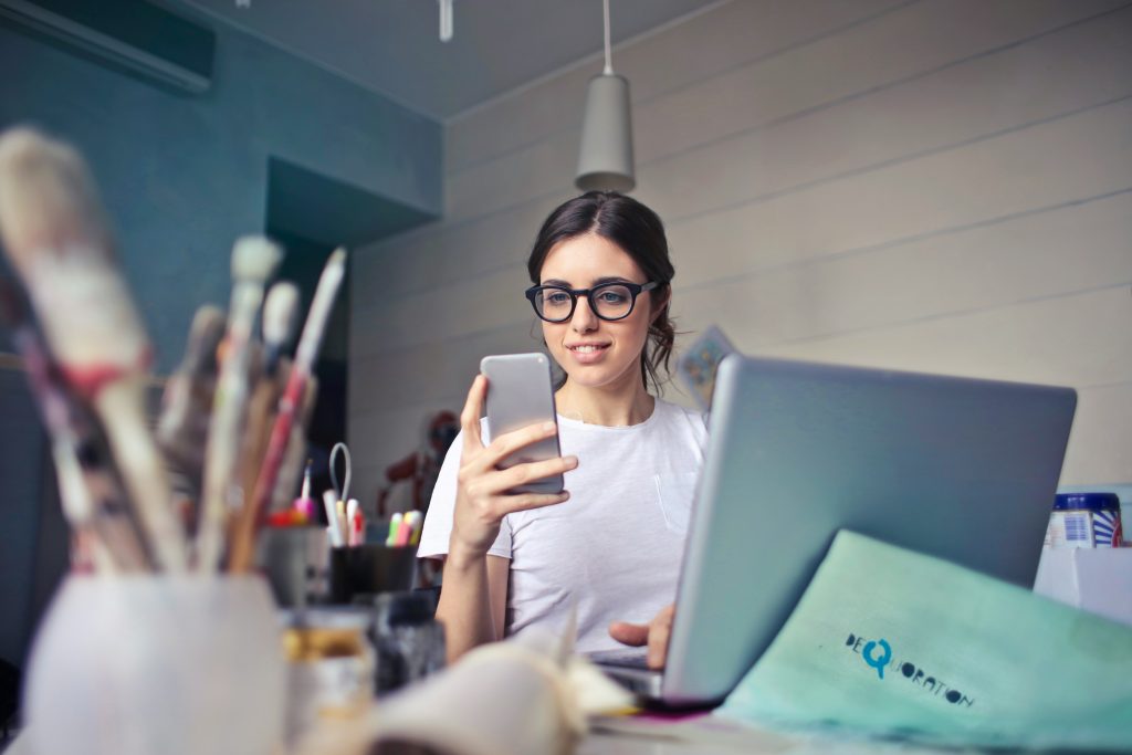 A girl with glasses sitting at her desk and looking at her I phone