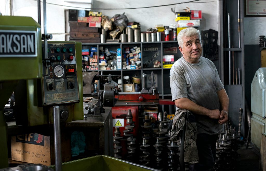 A man standing in a workshop next to a machine, surrounded by tools and equipment.