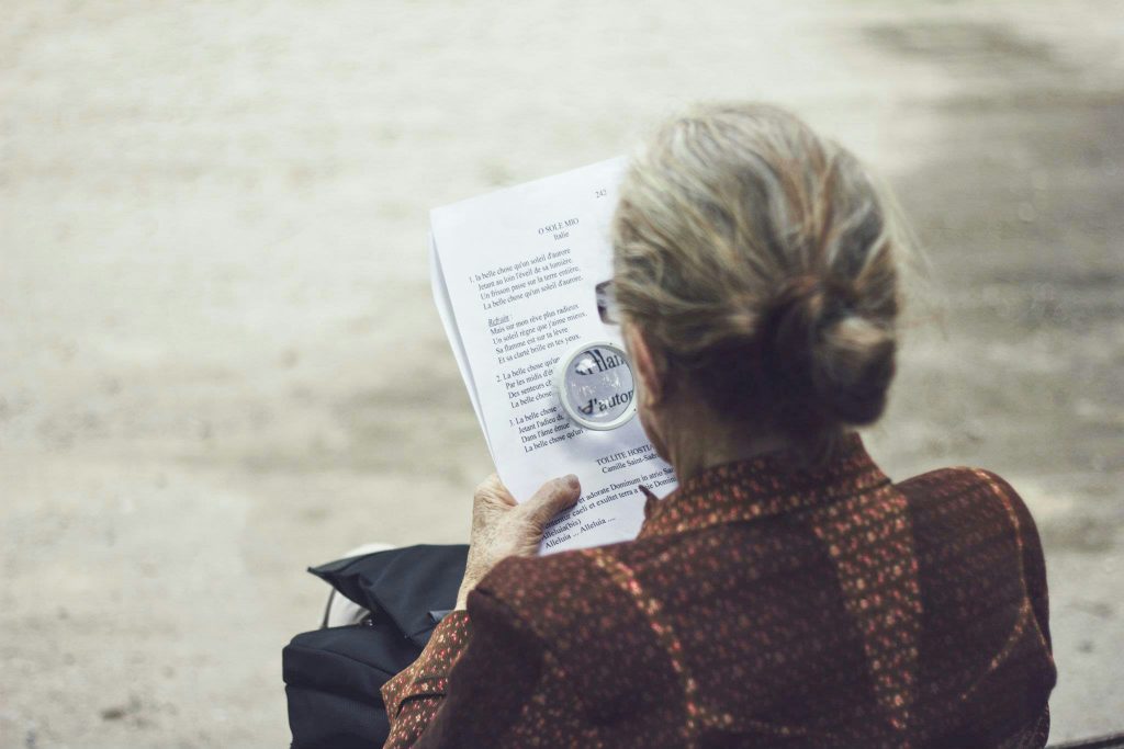 back of an old woman reading with a magnifying lens